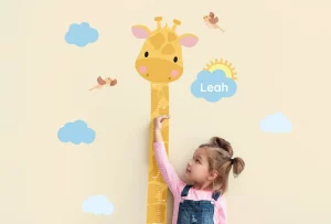 Barn der måler sin højde på en højdemåler med girafmotiv og navnet “Leah”.