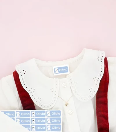 Barnesko og børnekjole med navnemærker placeret på tøjet, omgivet af snefnug-dekoration.