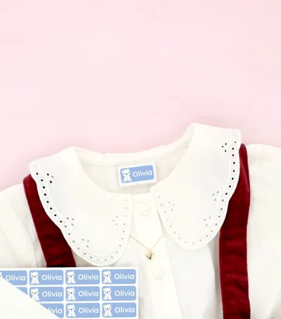 Barnesko og børnekjole med navnemærker placeret på tøjet, omgivet af snefnug-dekoration.