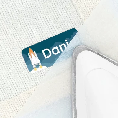 Strygbar navnelap med raketmotiv, der viser et navn på tekstil, ideel til personliggørelse af børnetøj.