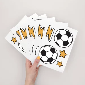 Hånd, der holder et sæt farverige klistermærker med fodbold, lyn og stjerner, perfekte til dekoration af børneværelser eller til personliggørelse af skoleartikler.