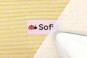 Navnelap med navn Sofia og en sød marihøne, placeret på et strikket stof. Produktet er ideelt til navnelabels til børnetøj, som gør det let at identificere personlige ejendele.
