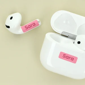 Navnelapper til airpods med navnet Sara i pink farve, placeret ved siden af en hvid opladeretui. Disse personlige navnelapper er perfekte til at holde styr på øretelefoner og tilføje et personligt præg.